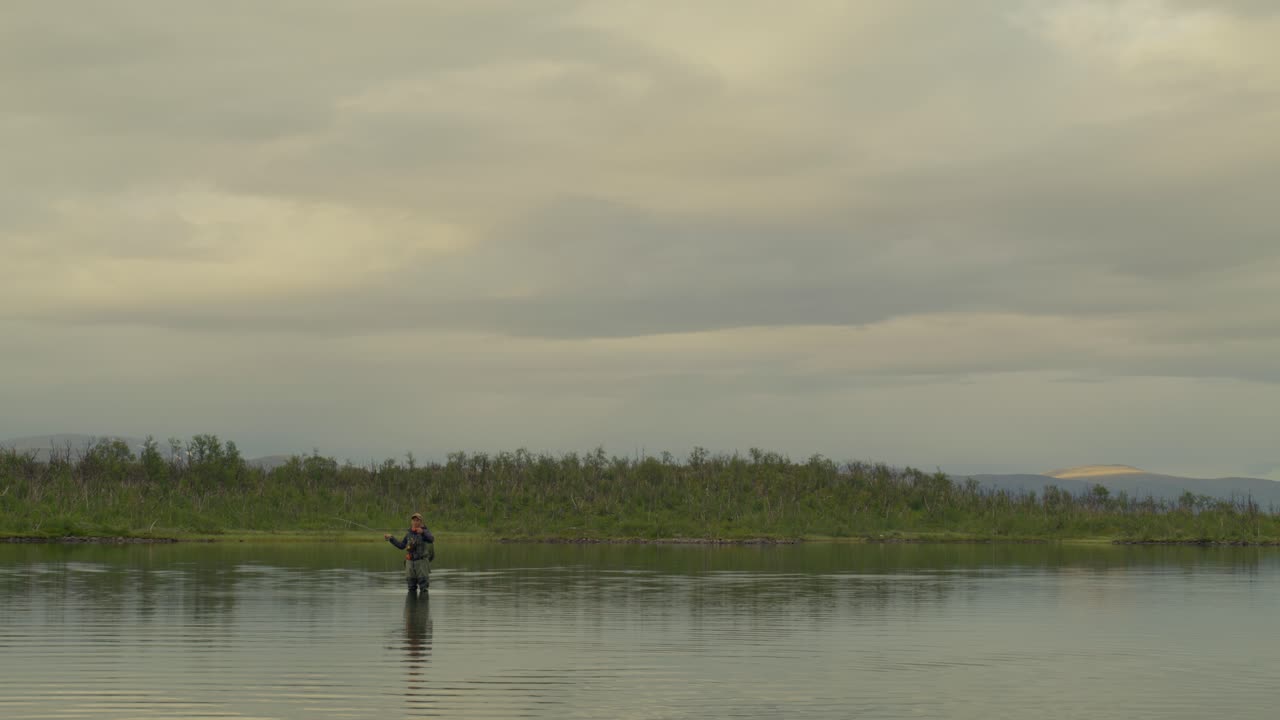 Wide frontal view of man fly fishing in still lake in northern Sweden