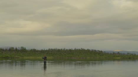 wide frontal view of man fly fishing in still lake in northern sweden
