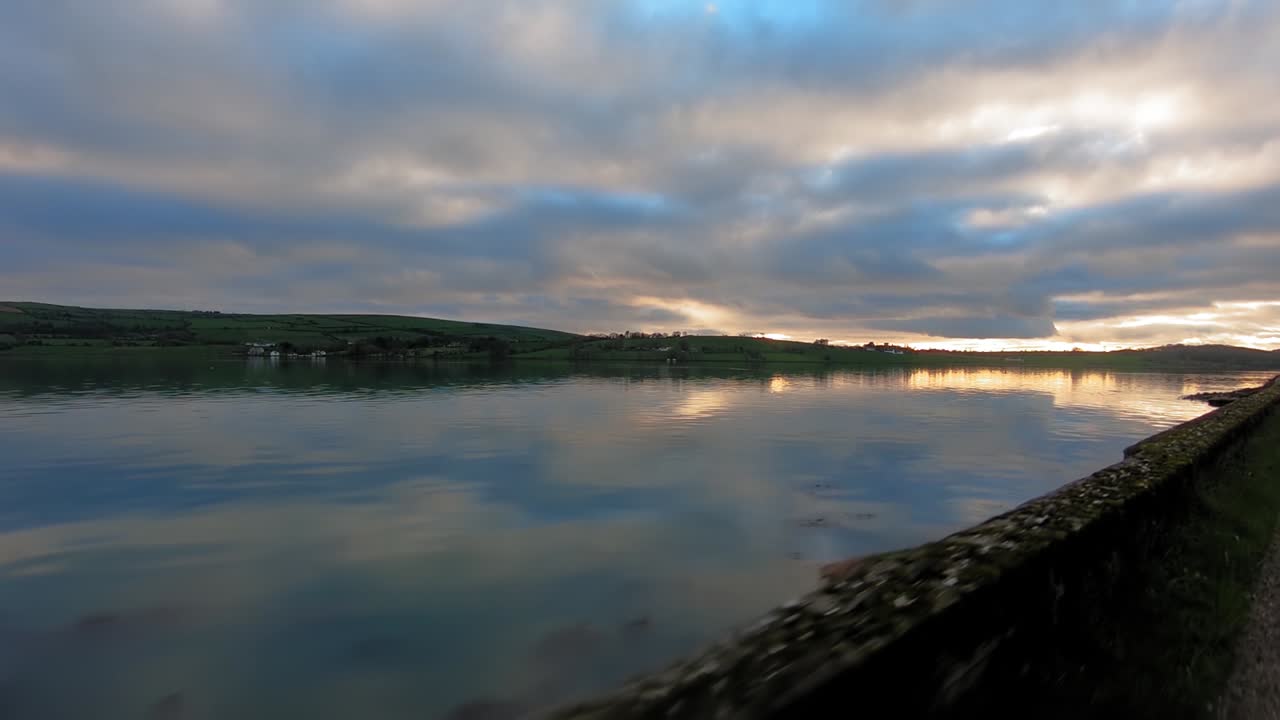 Driving along side Ireland river during sun set beside stone wall