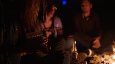 two boys and two girls sitting by the fire at night and singing songs. happy friends singing songs and playing guitar, talking