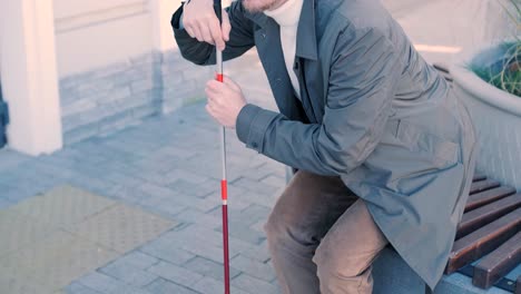 blind person using white cane on straight tactile tiles to navigate road