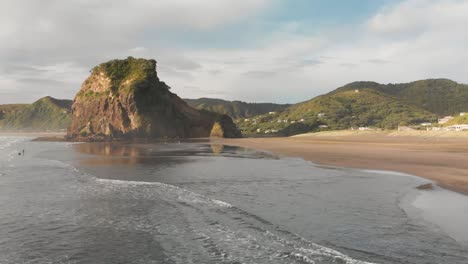 aerial drone shot flying over waves towards beatiful lion rock on piha beach, new zealand