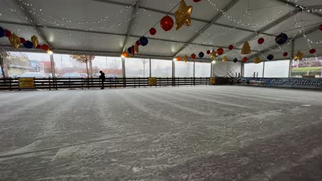 Little-girl-skating-on-ice-alone-in-empty-indoor-ice-rink-with-Christmas-decorations-hanging-on-ceiling