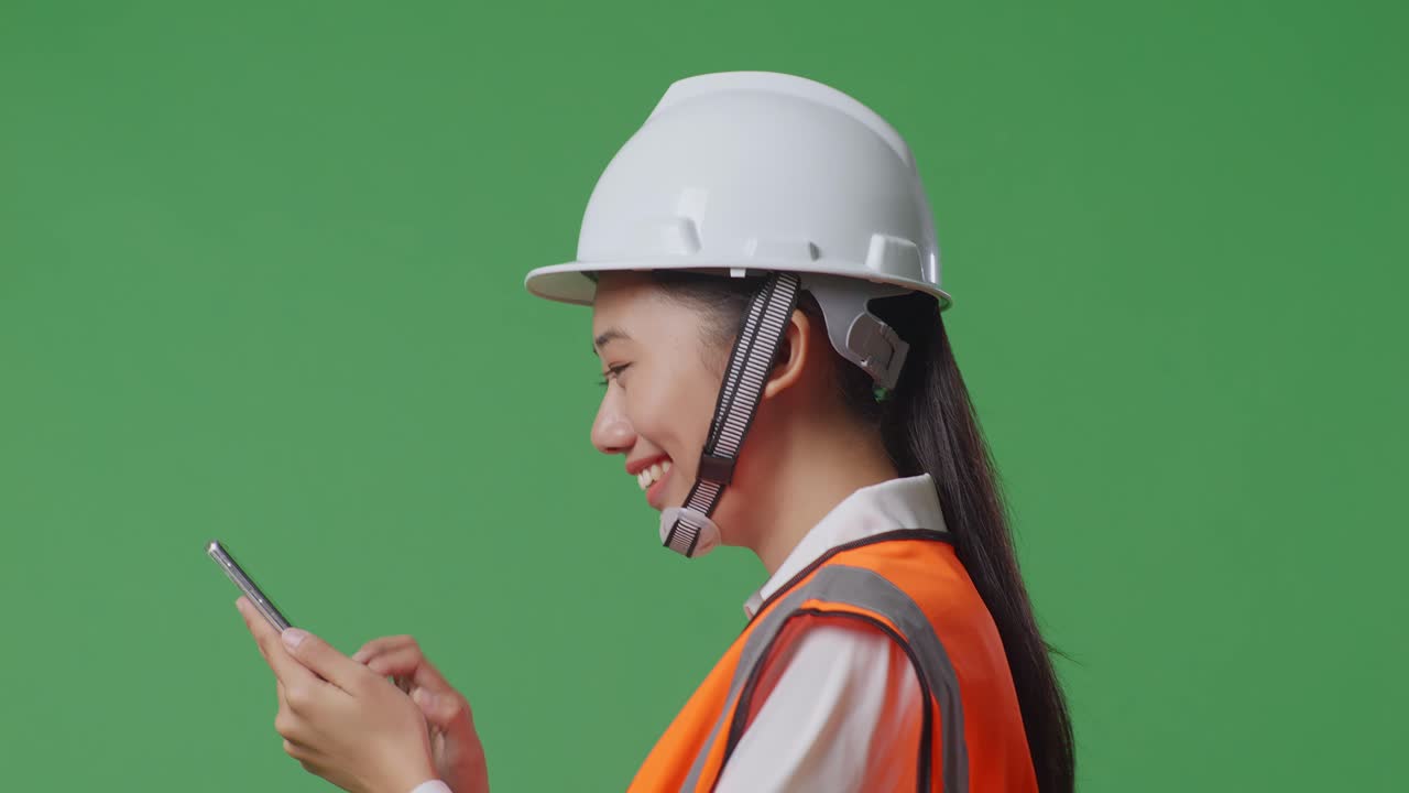 녹색 스크린 배경 스튜디오에서 는 동안 스마트폰을 사용하는 안전 헬을 입은 아시아 여성 엔지니어
