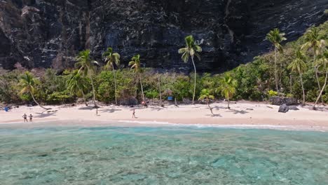 Aerial-trucking-shot-of-tourist-resting-on-PLAYA-FRONTON-in-front-of-steep-mountain,Dominican-Republic