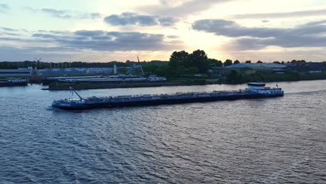 cargo ship sails at sunset near dordrecht, calm river reflecting light