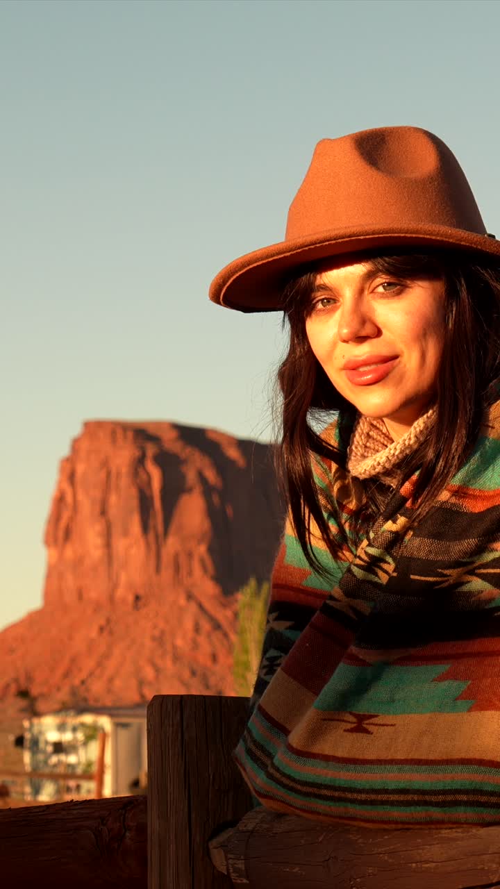 Giovane donna con cappello e poncho che sorride in un paesaggio desertico al tramonto