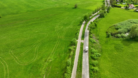 A-top-down-aerial-view-of-a-winding-road-in-the-countryside,-with-a-camper-driving-along-it