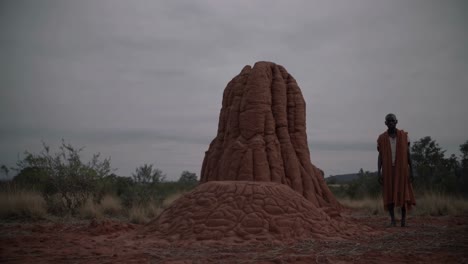 local man wearing traditional clothing stands beside a giant termite mound in the african savanna, capturing the region's unique natural wonders and cultural essence