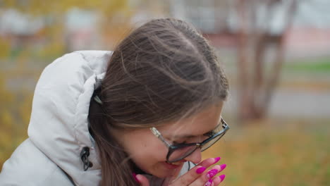 close up of smiling young woman in glasses nodding her head with excitement as wind gently blows her long hair surrounded by soft autumn tones and blurred golden trees