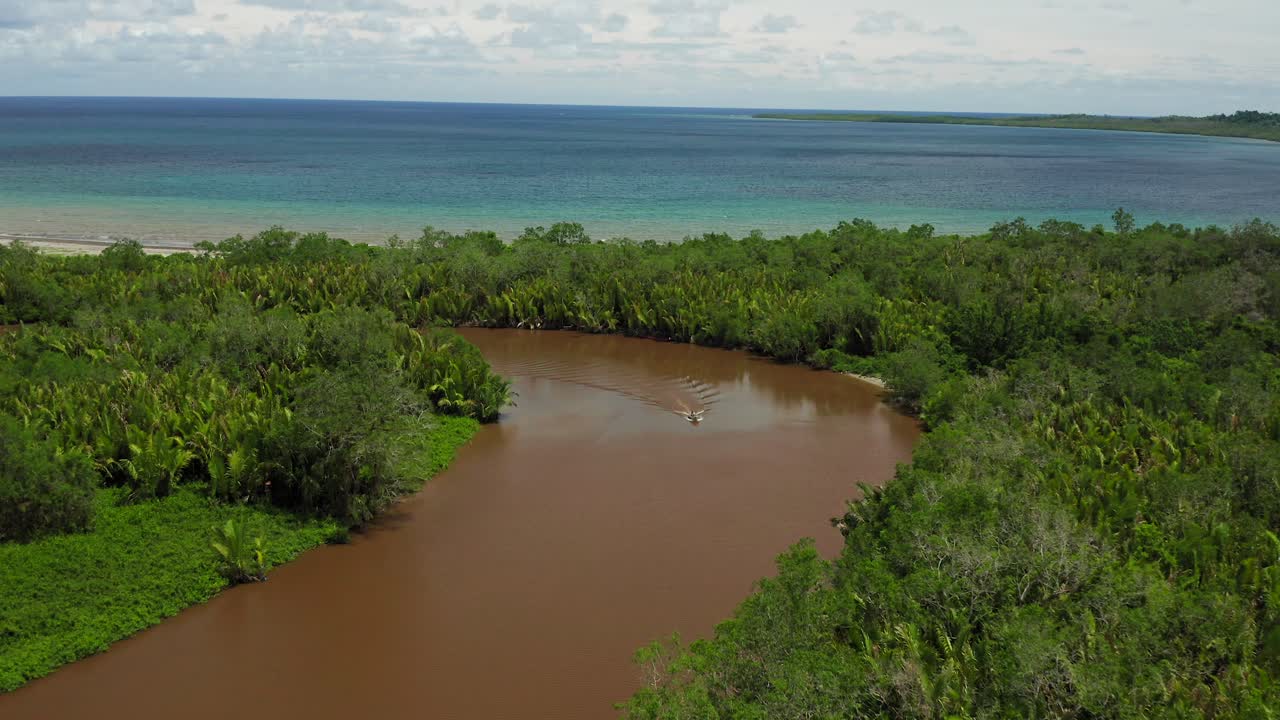 Aerial crane shot of boat in murky Indonesian river with blue ocean horizon