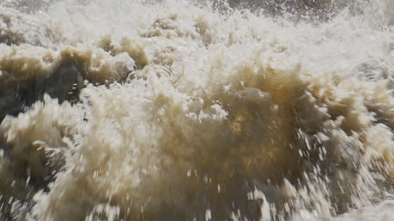 Raging white water churns violently, splashing everywhere. Foam and spray create chaotic motion across turbulent surface. This intense scene captures raw power of nature