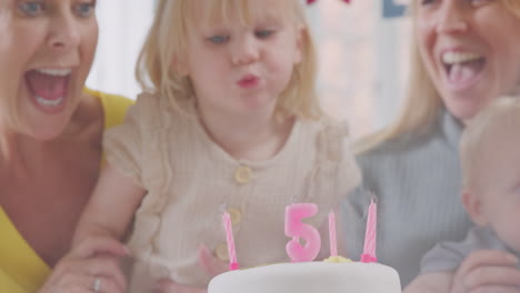 nieta soplando velas en el pastel con la madre y los abuelos en la fiesta de cumpleaños