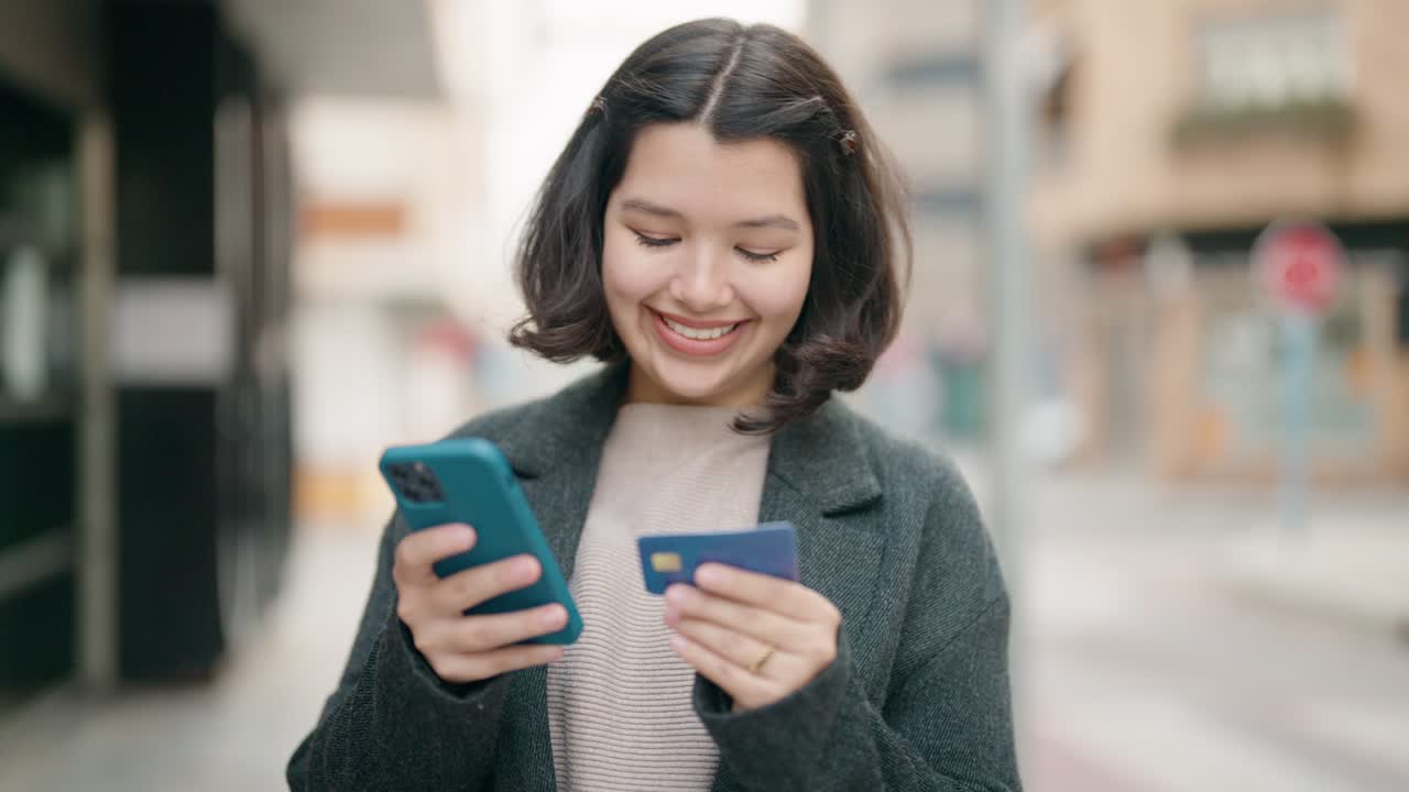 joven hispana usando teléfono inteligente y tarjeta de crédito en la calle