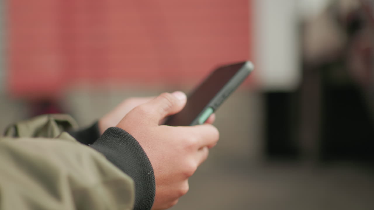 Close up hand view of kid in jacket sliding through smartphone screen outdoors, showing fingers engaged with device against blurred background