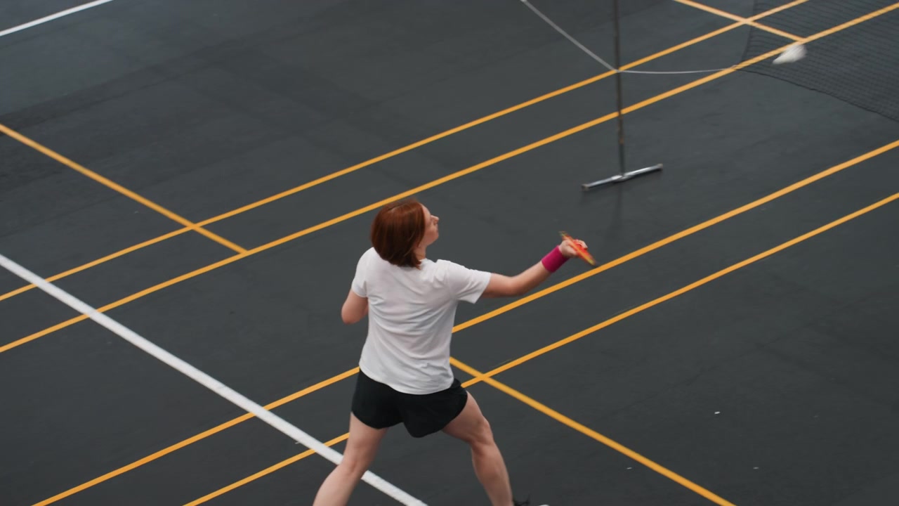 Overhead indoor court woman practicing badminton drill, steady lowtohigh returns and controlled swings, focus on footwork, balance and consistent shuttle placement during training session