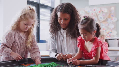 two schoolgirls at a sensory play table with female teacher in an infant school classroom, close up