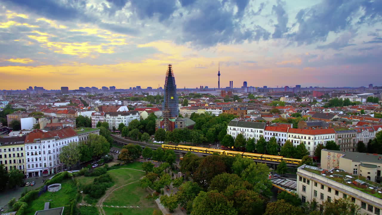 Aerial drone view of Kreuzberg, Berlin at sunset, Germany. Residential district with greenery, buildings and Berlin Television Tower in the distance, moving trains
