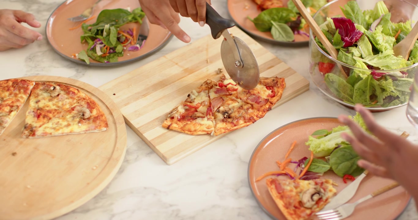 Amici afroamericani che condividono una pizza, la donna a destra solleva una fetta mentre gli altri tagliano, spazio per il testo.