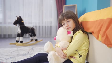 una niña infeliz y pensativa abrazando a su oso de peluche en su habitación.