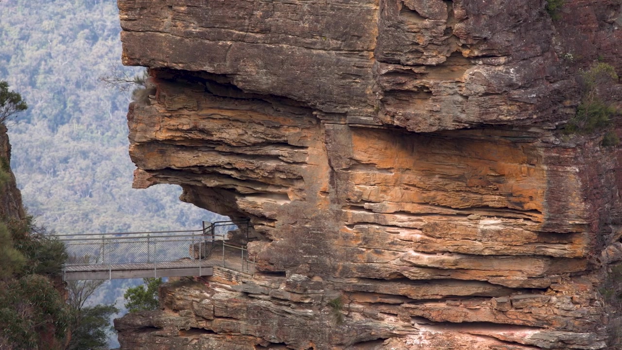 Static shot of Honeymoon Bridge connecting to a rugged sandstone cliff in Blue Mountains, Australia.