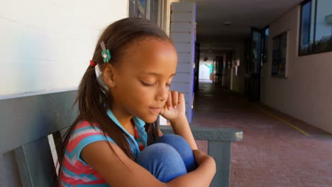 side view of african american schoolgirl sitting on bench and crying in school corridor 4k