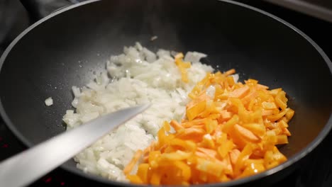 a female hand adds chopped carrots to finely chopped onions in a pan