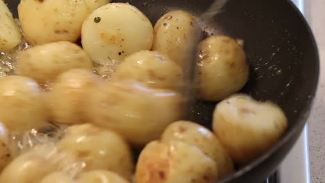 closeup of small potatoes being sautã©ed in a pan with bubbling butter, garlic and chopped herbs on a gas stove