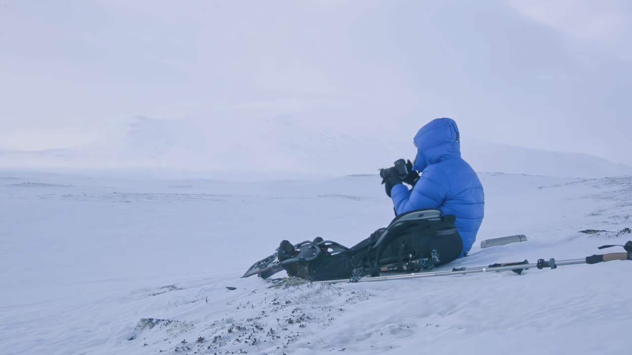 파란색 재을 입은 관광객이 노르웨이의 눈 인 산의 사진을 찍습니다.