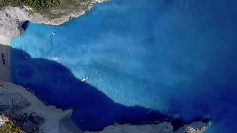 Aéreo:-Toma-De-Arriba-Hacia-Abajo-De-La-Playa-De-Navagio-En-Zakynthos,-Grecia,-Mientras-La-Playa-Está-A-La-Sombra