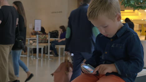 Niño-Mirando-Fotos-En-Un-Teléfono-Móvil-En-El-Centro-Comercial