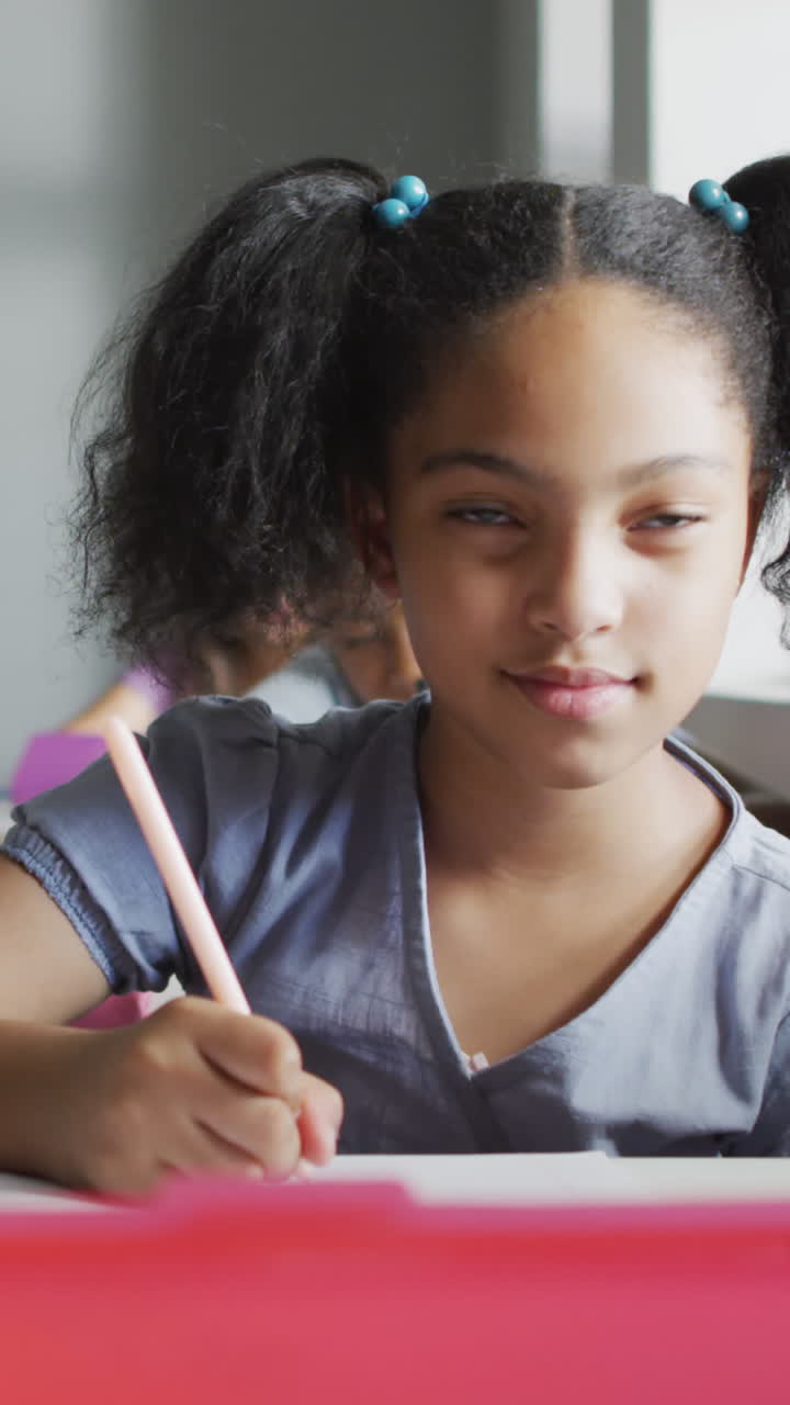 video de una chica biracial centrada sentada en un escritorio en el aula