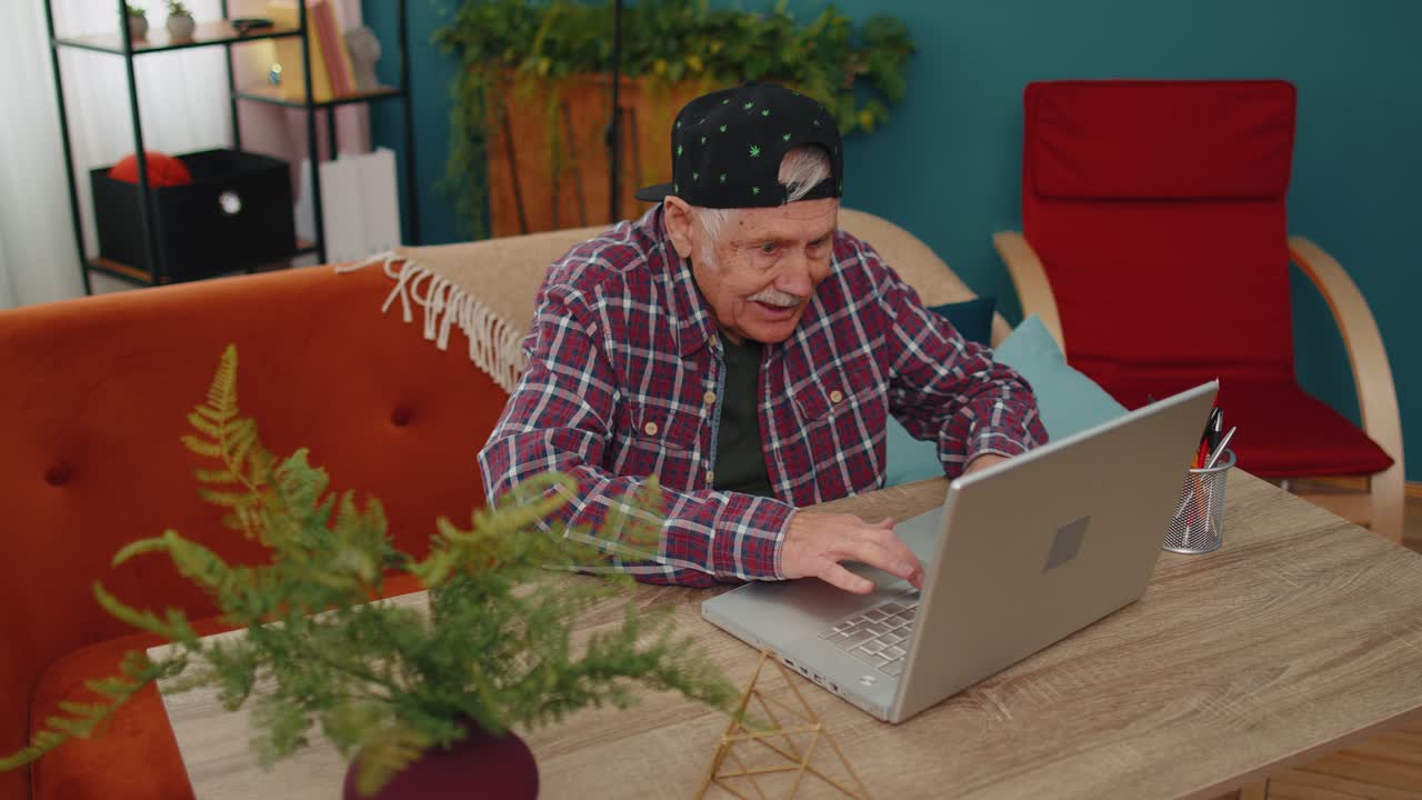 Grandfather man playing computer video games on laptop computer wins celebrate smiles happily