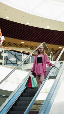 hermosa dama con una camiseta negra bajo un vestido rosa bajando una escalera mecánica sosteniendo bolsas de compras en su mano izquierda mientras su mano derecha está en el carril, los juguetes y otros artículos son visibles arriba