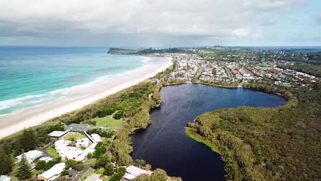 drone flying in sideways arc showing freshwater tea-tree stained lake, adjacent beach and headland in background