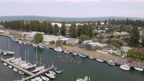 Aerial-top-down-shot-of-stand-up-paddlers-paddling-between-boats-in-harbor-of-Port-Fairy,-Australia