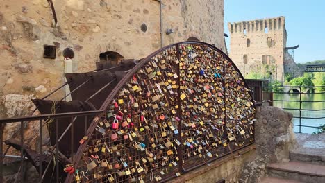 Love-padlocks-on-fence-of-metal-water-wheel-turbine-in-Borghetto-Verona-Italy