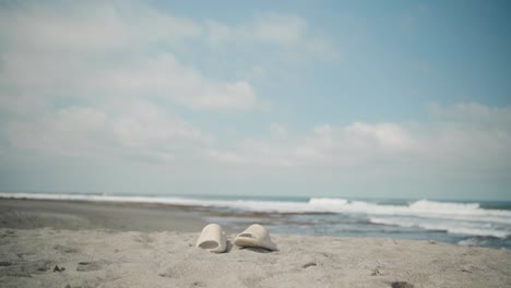 Cream-Sandals-Left-Behind-on-a-Beach-with-Ocean-Waves-in-the-Background