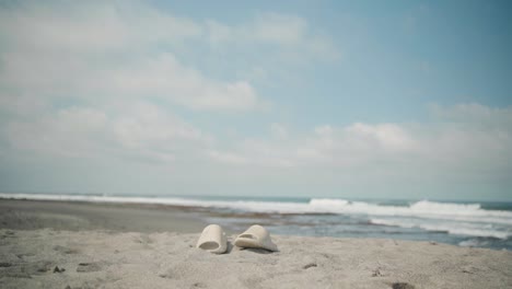 sandalias de crema dejadas en una playa con olas del océano en el fondo