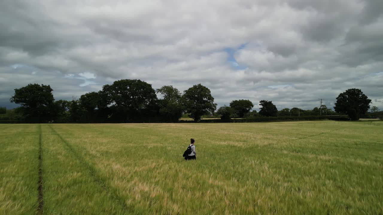 Woman walking solemnly through field of wheat - drone pan and follow on a typical English summer’s afternoon