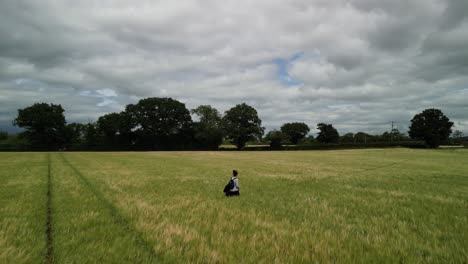 woman walking solemnly through field of wheat - drone pan and follow on a typical english summer’s afternoon