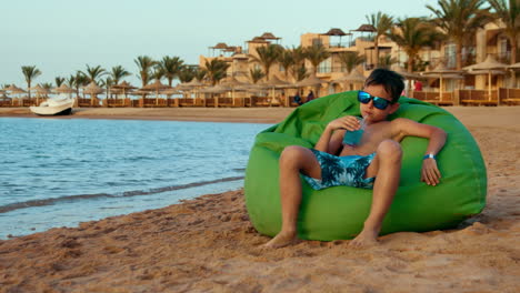 teenage boy enjoying lemonade at coastline. cute young man sitting at seaside.