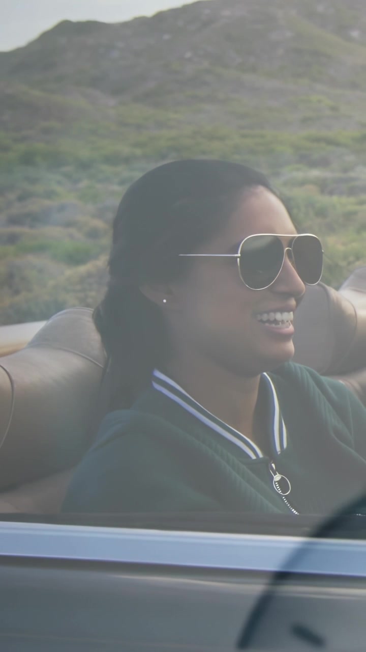 Vertical video: Woman laughing head toss causing clock-glow turning arms up cheering open car ride