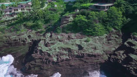 Aerial-view-of-rocky-cliffs-and-crashing-waves-revealing-luxury-homes
