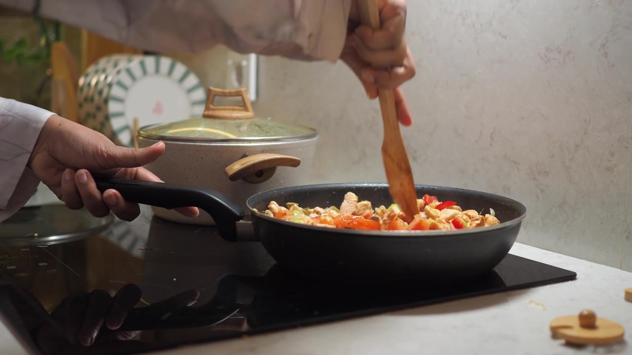 Chef removiendo verduras frescas y pollo en una sartén