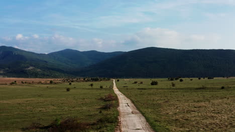 Cámara-Aérea-Moviéndose-A-Lo-Largo-De-Un-Largo-Camino-A-Través-De-Un-Amplio-Campo-Con-Un-Hermoso-Paisaje-Montañoso