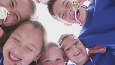 low angle view looking up into faces of children in huddle on sports day holding medals