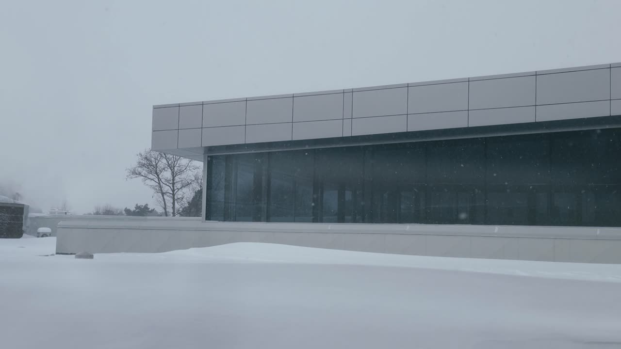 Snø føyker forbi store vinduer på et bygningstak med eksos i bakgrunnen
