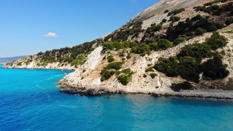 blue calm waves by the agia kiriaki beach and lush cliffs in greece - aerial pullback