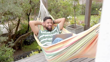 relaxing in hammock, man smiling and using laptop in backyard garden
